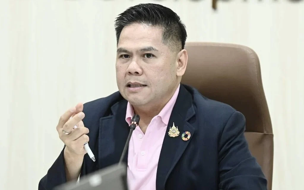 A minister speaks at a meeting, seated behind a desk.