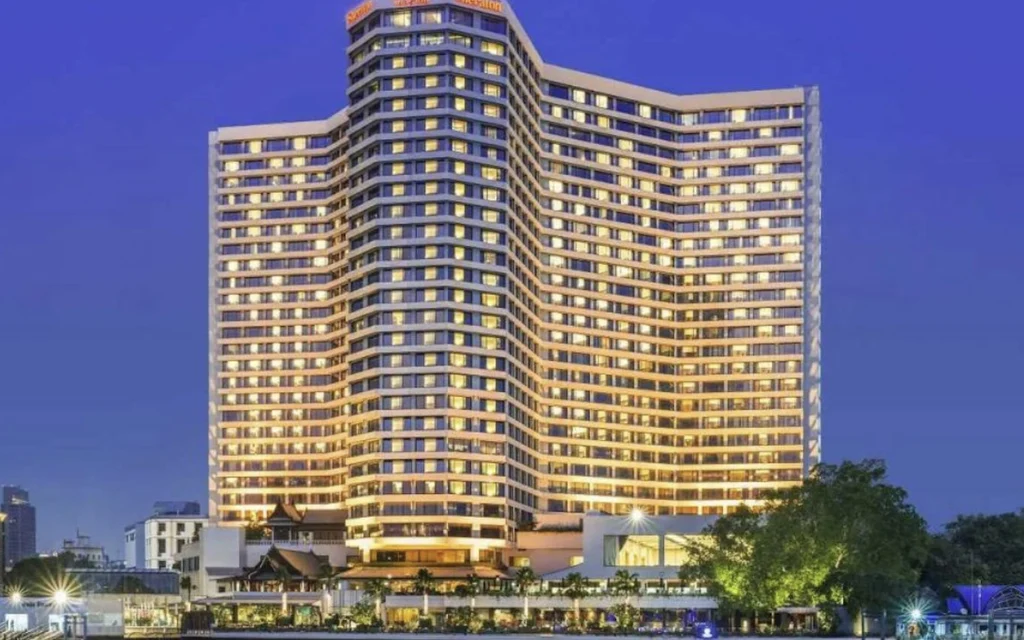Illuminated Royal Orchid Sheraton hotel beside a river at dusk