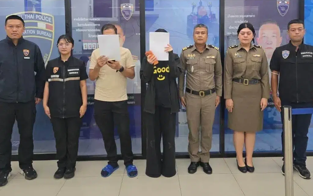 Thai immigration police officers standing with two suspects covering their faces.
