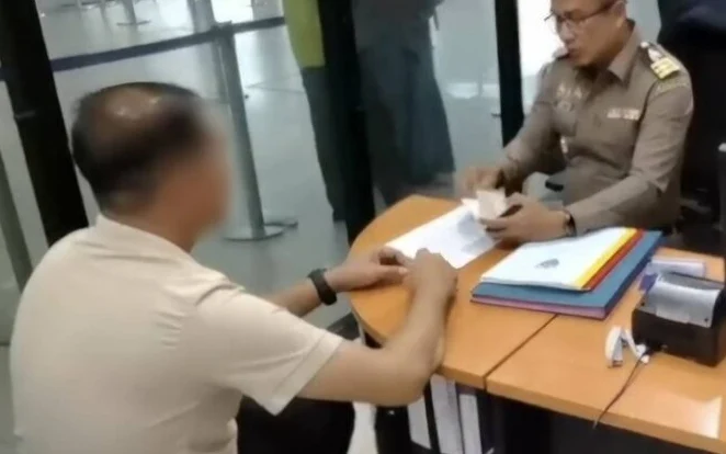 An immigration officer reviewing documents with a person at a desk.