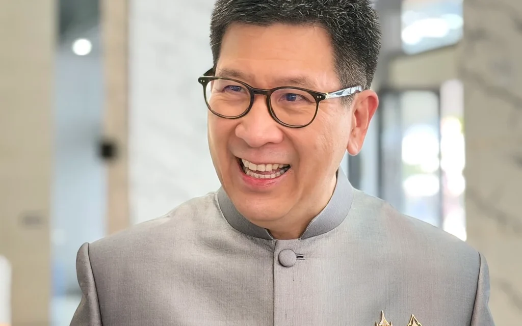 Smiling man wearing glasses and a gray formal jacket with pins.