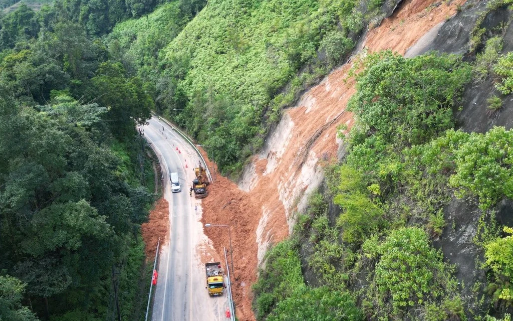 Aerial view of a landslide blocking a winding road through forested hills.