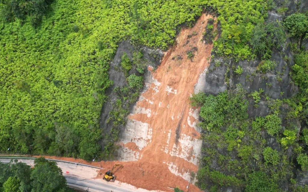 Aerial view of a landslide blocking a road through forested terrain.