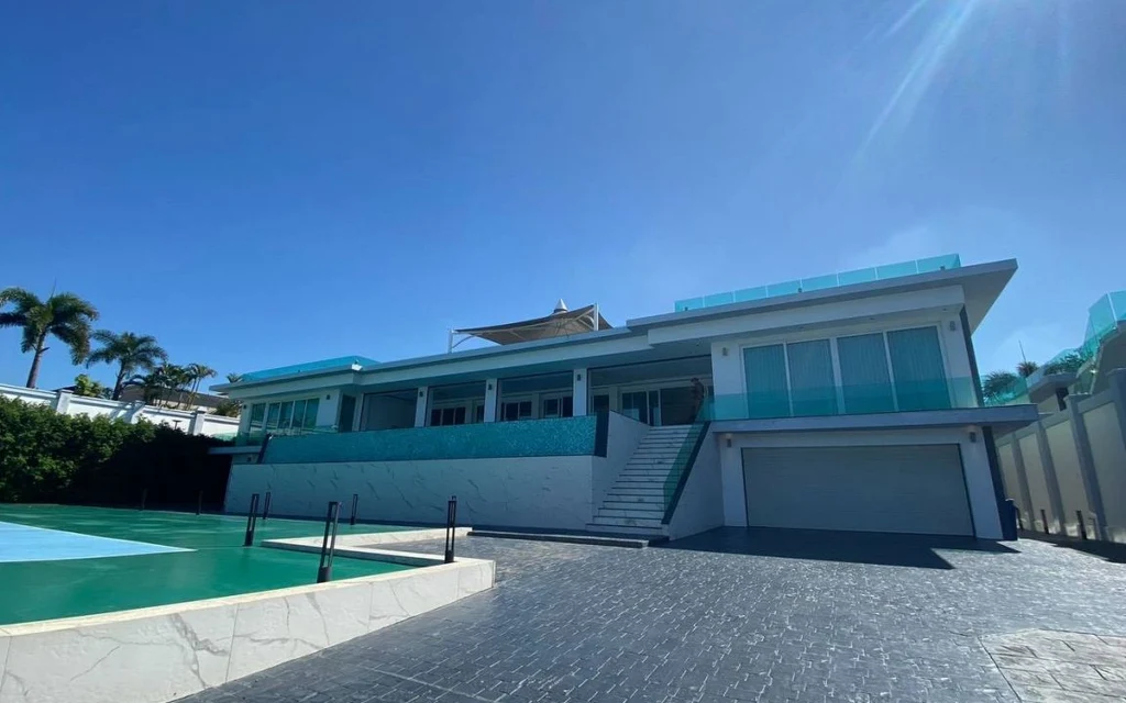 Modern villa with swimming pool and paved driveway under bright sunlight.