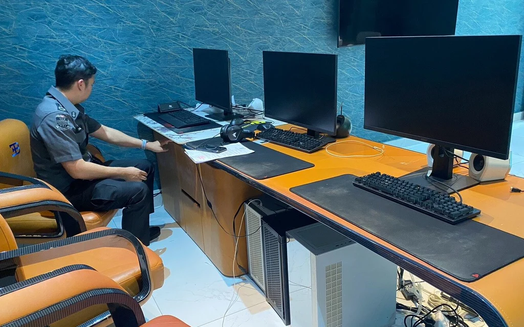 A uniformed officer sits beside computer equipment in an office.