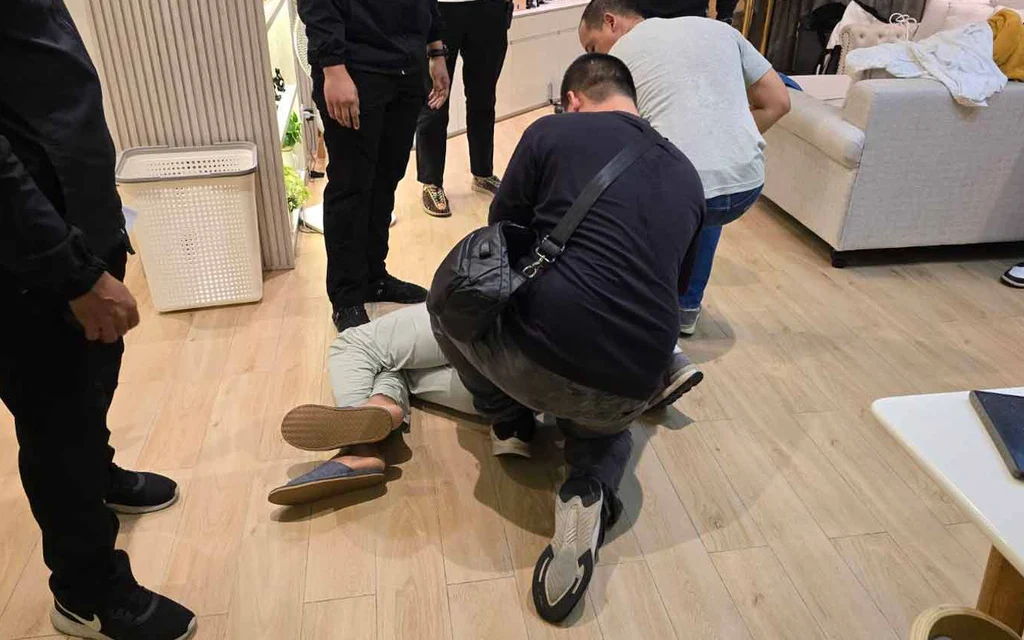 Police detain a man on the floor inside a Bangkok residence.