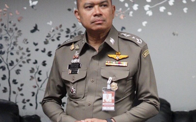 A Thai immigration police officer in uniform standing indoors.