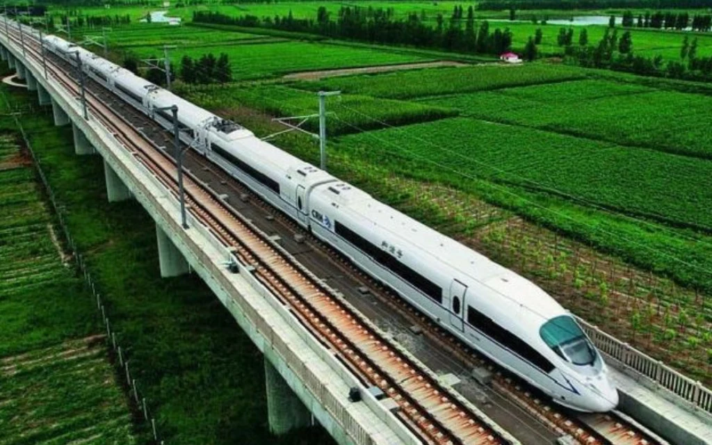 A high-speed train traveling on an elevated track through rural fields.