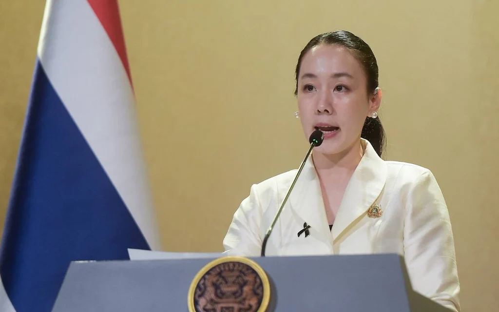Woman speaking at a podium beside the Thai flag