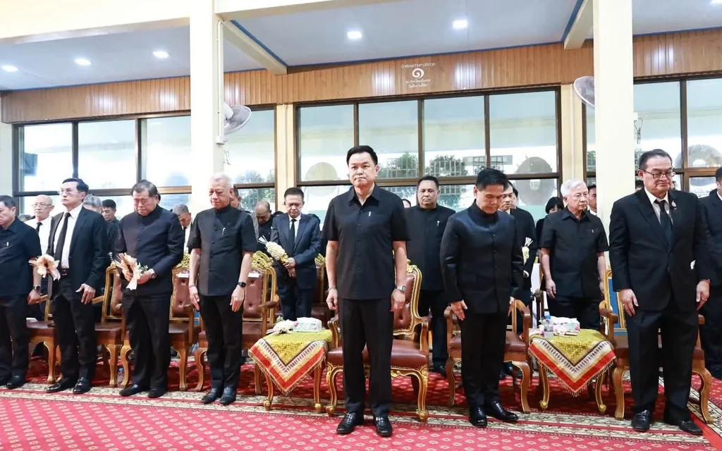 Officials stand at a funeral ceremony in a decorated indoor hall.
