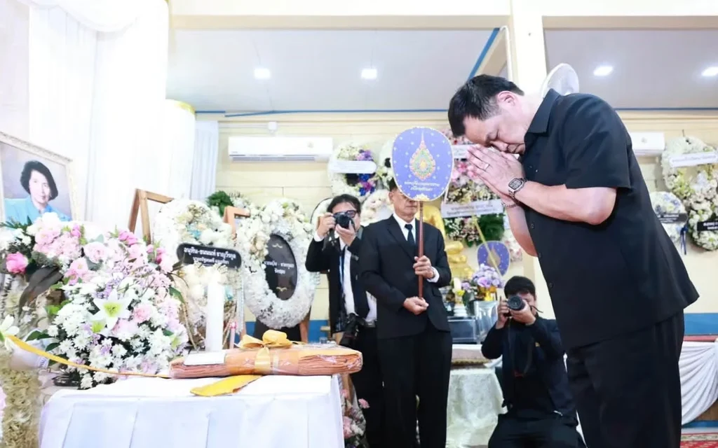 A man pays respects at a funeral ceremony beside a flower-covered altar.