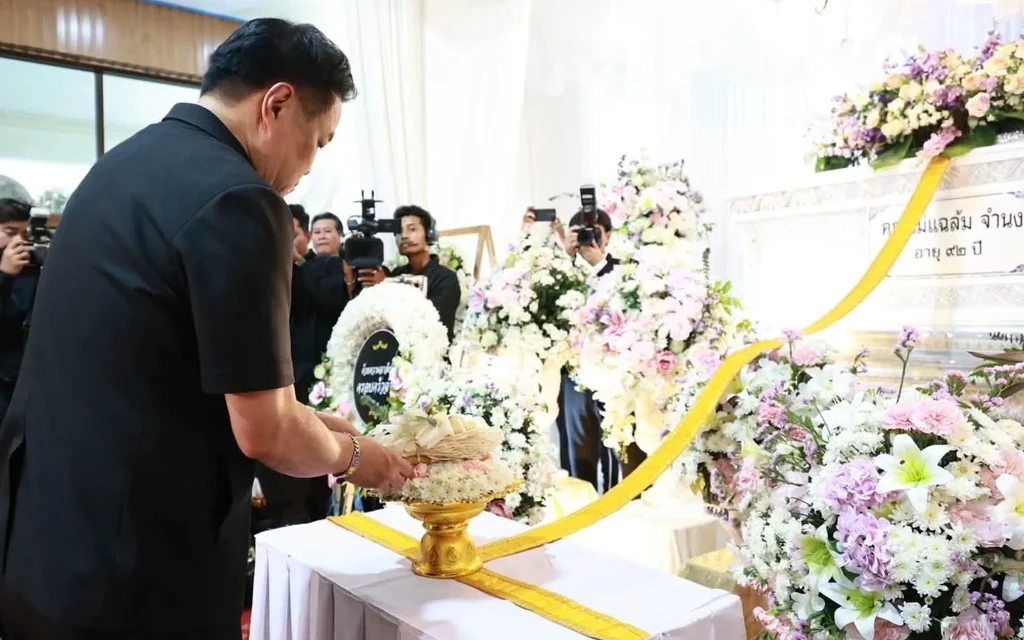 A man places a floral offering beside a funeral altar as photographers watch.