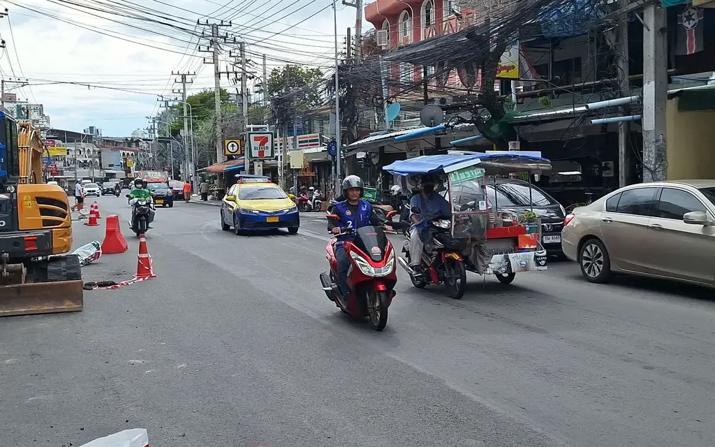 Motorcycles and cars travel along a busy street with road construction.