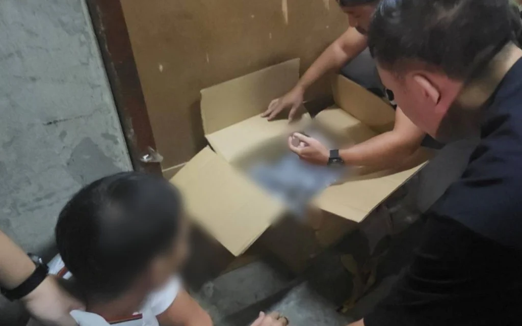 Officers inspect a box during a drug raid; one person’s face is blurred.