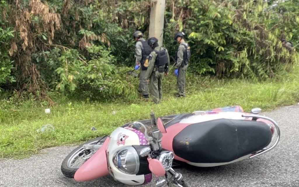 Police officers inspect a fallen scooter beside a rural road.