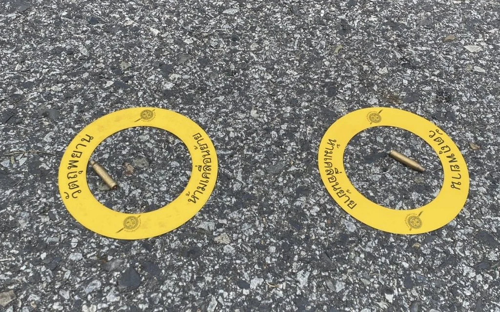 Two yellow evidence markers surround spent shell casings on asphalt.
