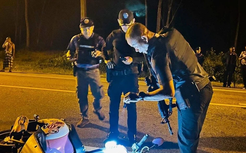 Police inspect a fallen motorcycle at a nighttime roadside scene.