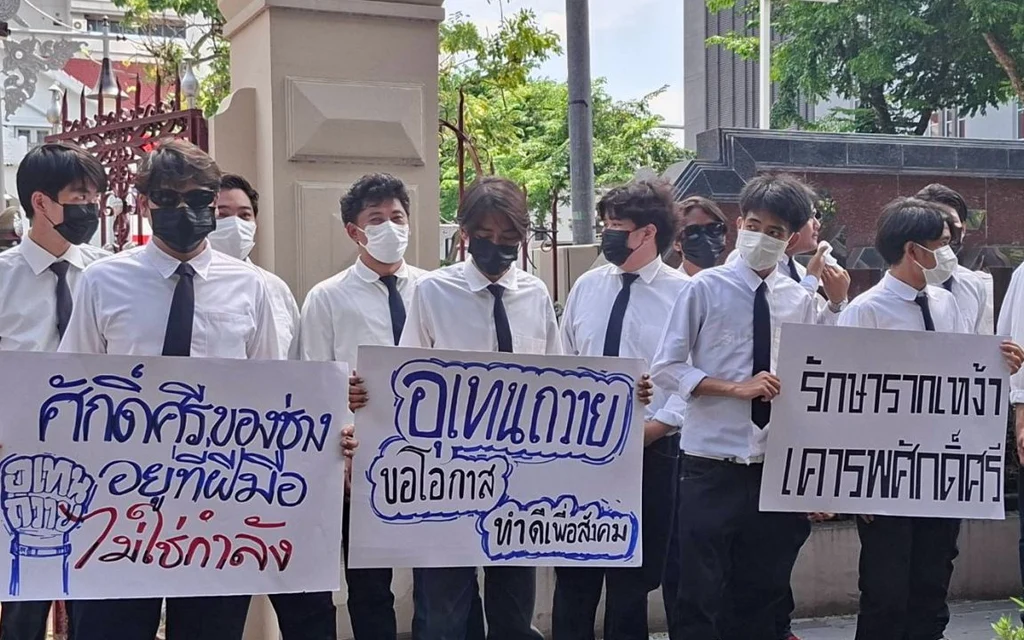 Masked students hold signs at a peaceful demonstration outside a building.