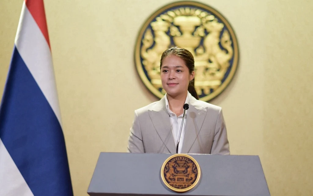 Female minister standing at a podium with the Royal Coat of Arms