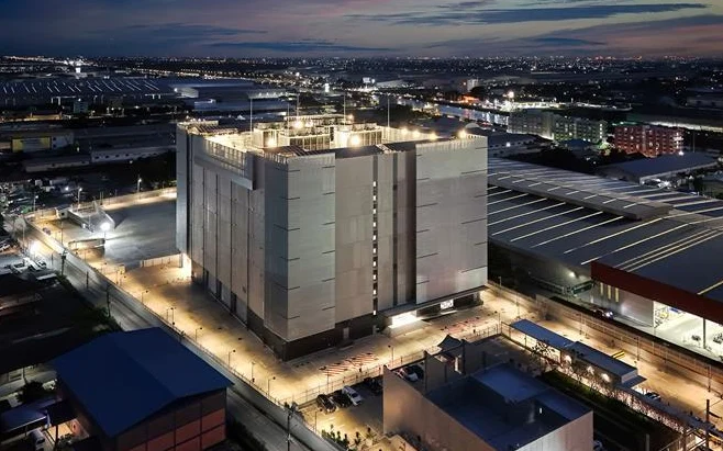 A large industrial facility illuminated at dusk in a sprawling business district.