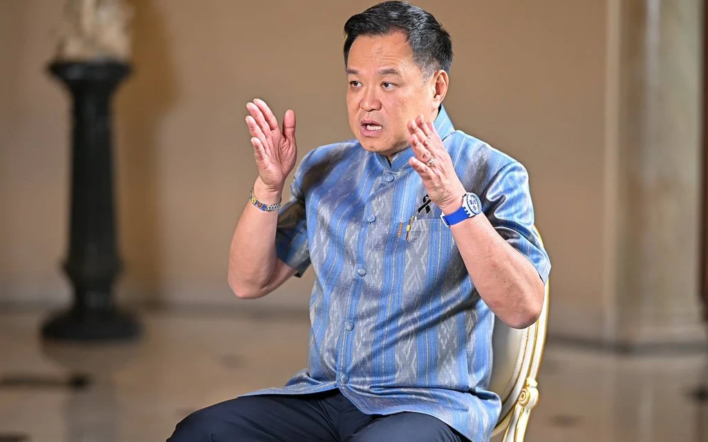 A man in a blue shirt gestures while seated indoors.