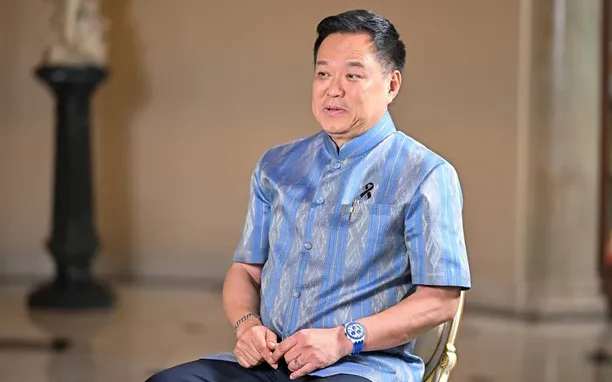 A man in a blue traditional-style shirt sits for an interview.