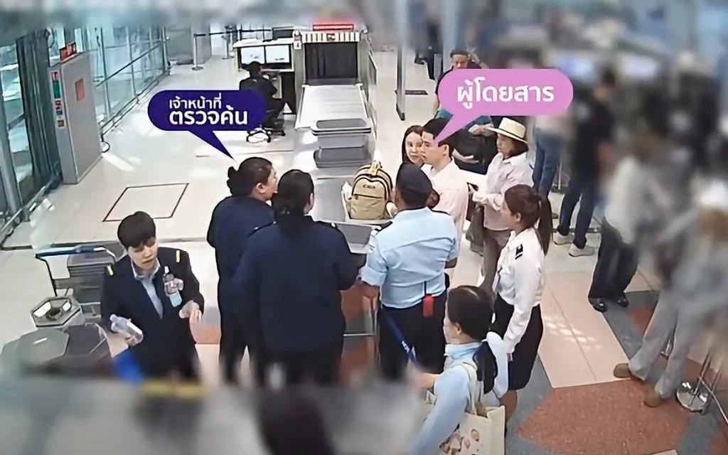 Airport staff and passengers gather around a security screening checkpoint.